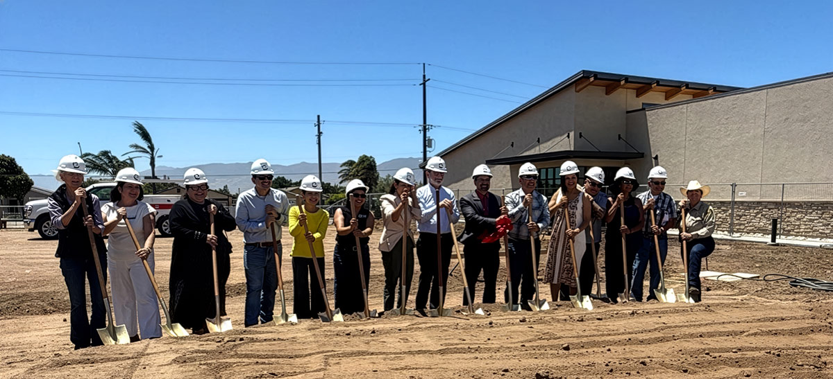 People wearing hard hats participate in the groundbreaking ceremony for Hartnell College's new Career Technical Education facility, standing in a row with ceremonial shovels at the construction site.