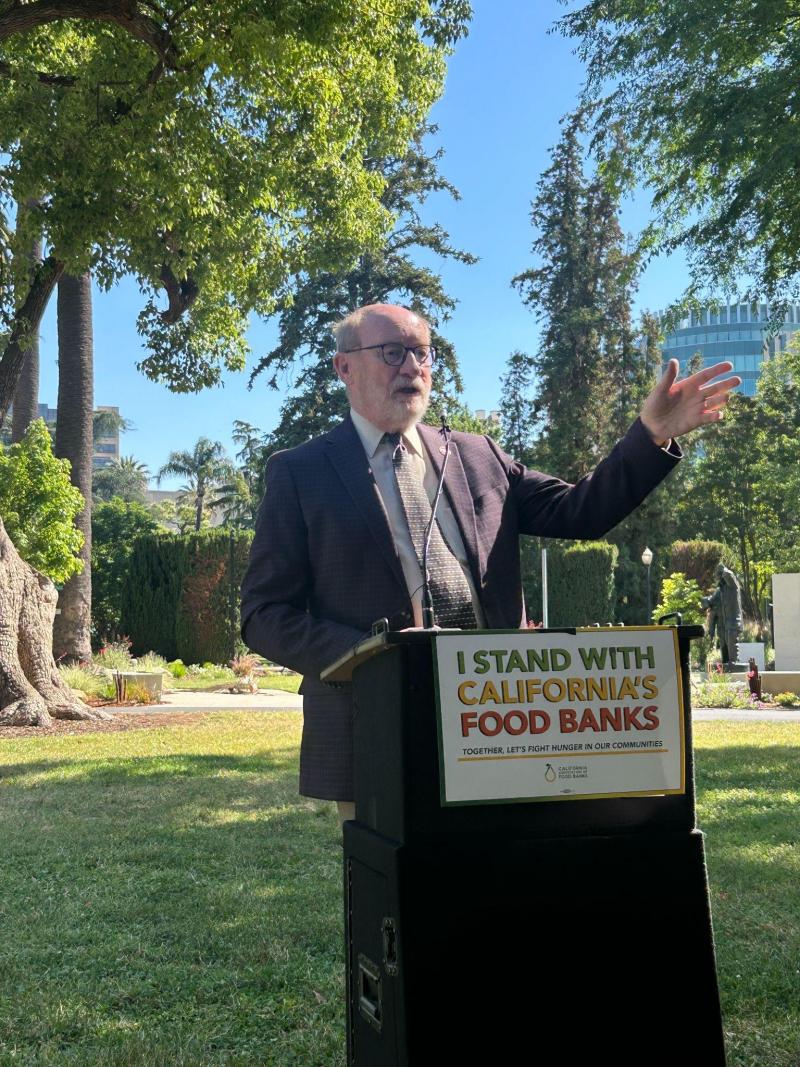 Senator Laird speaking behind a podium on the Capitol lawn in support of California food banks.