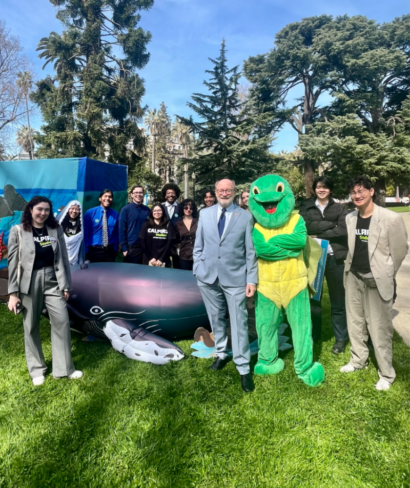 Senator Laird standing next to a costume turtle, inflatable whale, and University of California students