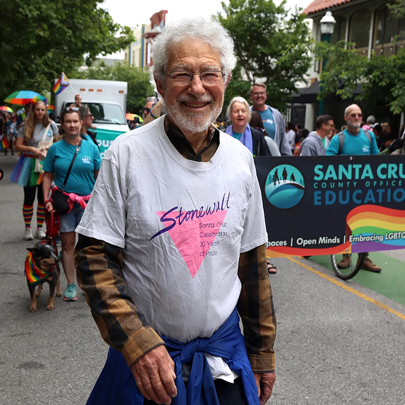 Mike Rotkin walking at a previous Santa Cruz pride, proudly wearing a Stonewell shirt as he walks alongside community members