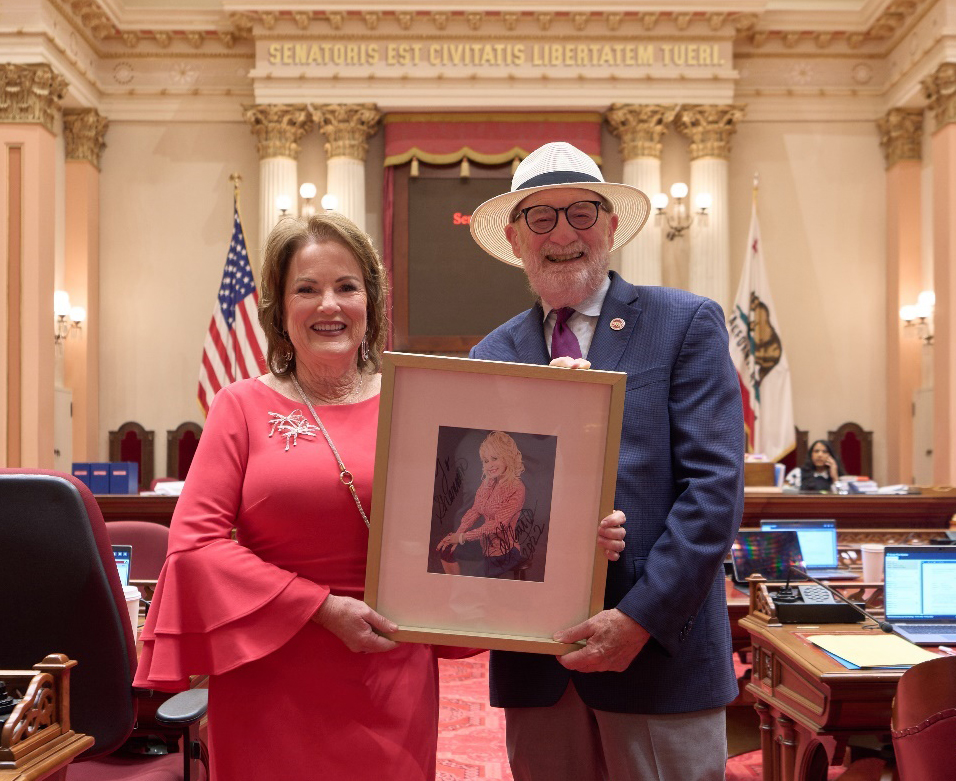 Senator Laird and Senator Grove on Senate floor holding Dolly Parton photo.