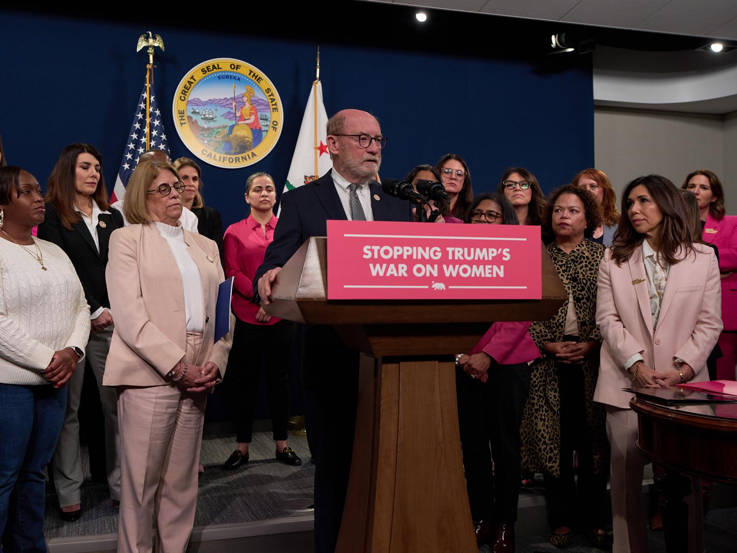Senator Laird speaking at a podium with the sign "Stopping Trump's War on Women"